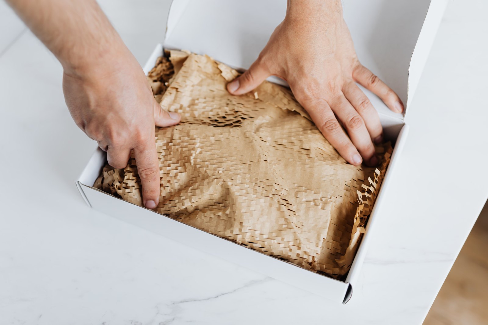 Handen pakken een bestelling in met beschermpapier op een lichte werktafel